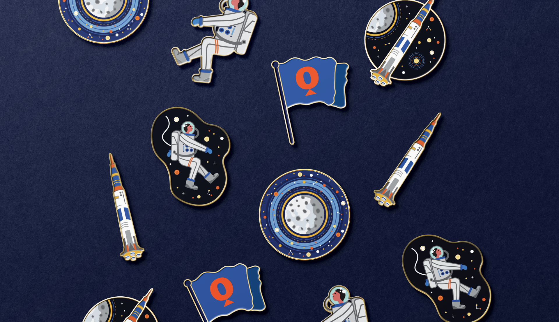 A mix of enamel pins laid out on a blue background. Enamel pins feature the moon, rocket, astronaut, and Questacon 'Q' flag.