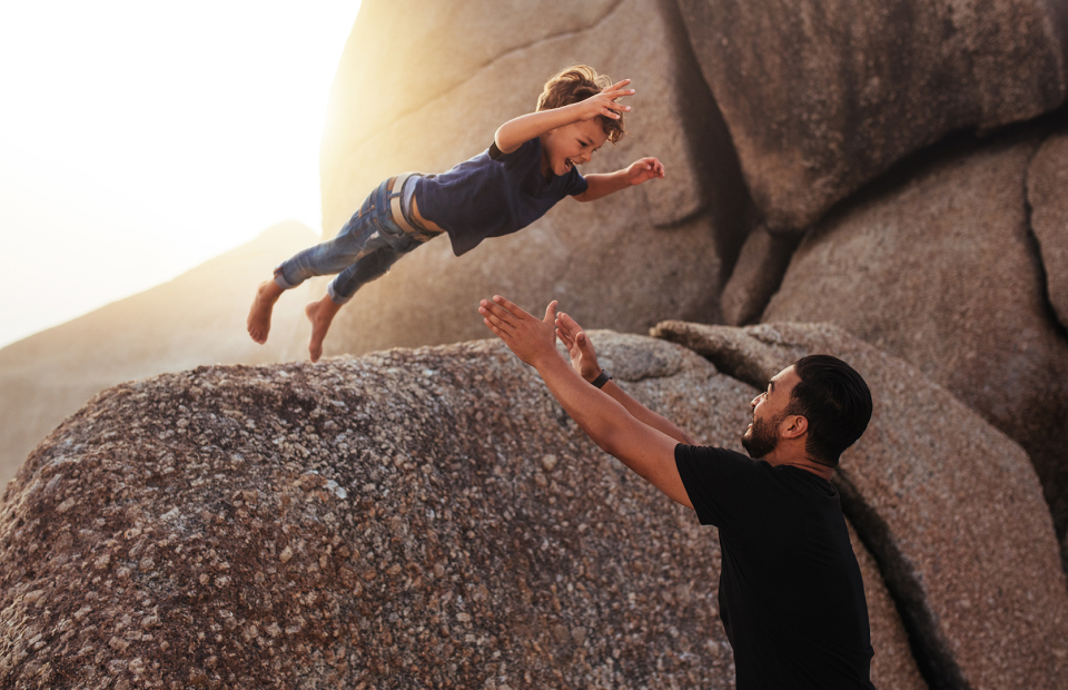 Child jumping off boulders into a father's arms. Sunflare behind.