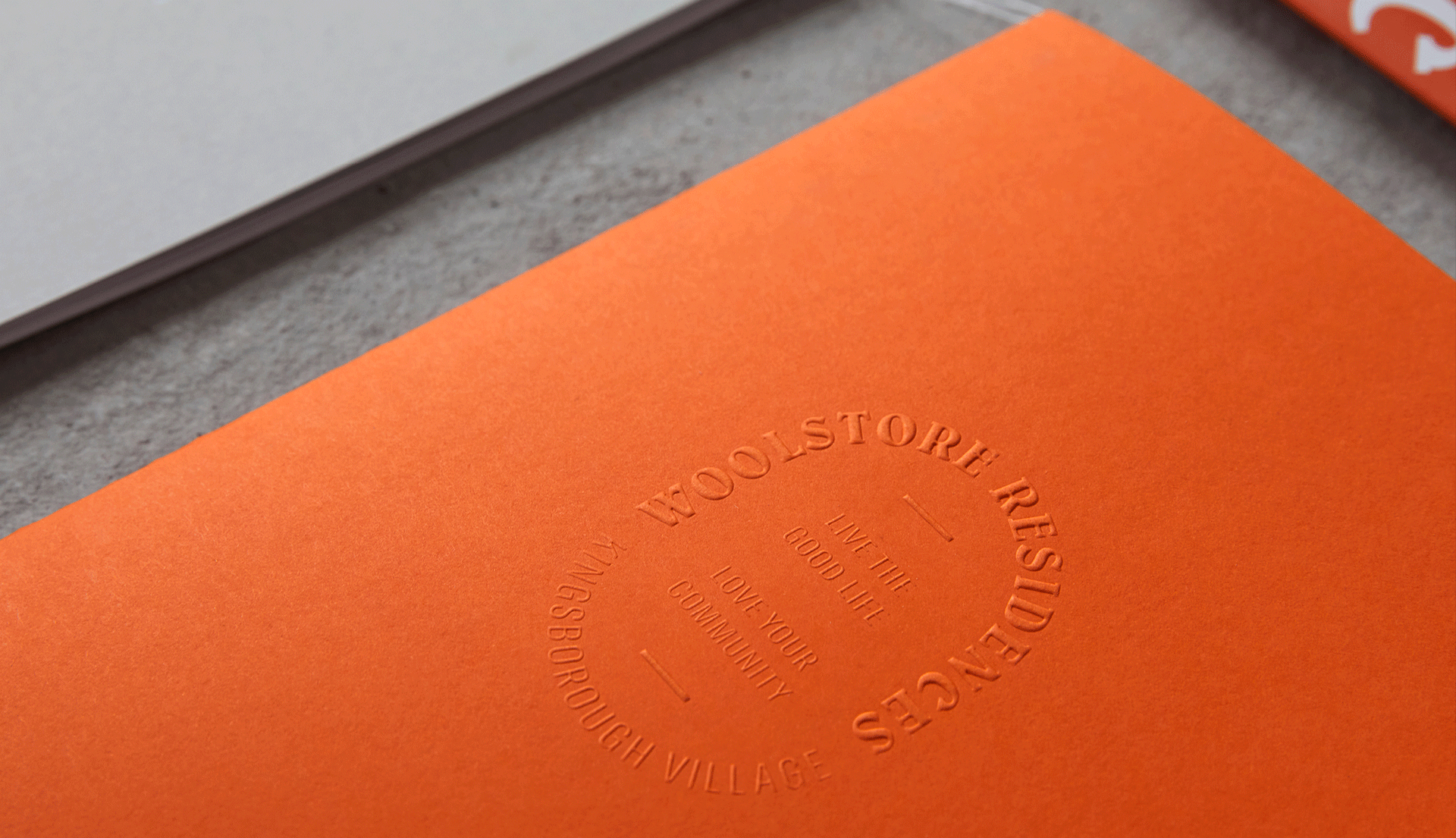 Close up photo of orange brochure cover with Woolstore Residences logo embossed.