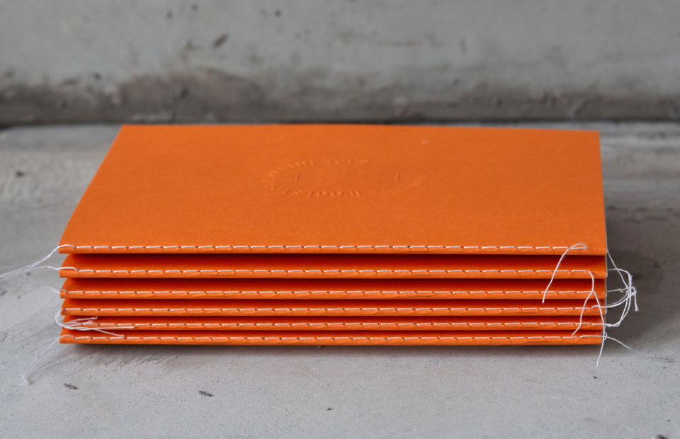 Stack of orange brochures showing stitched spine.