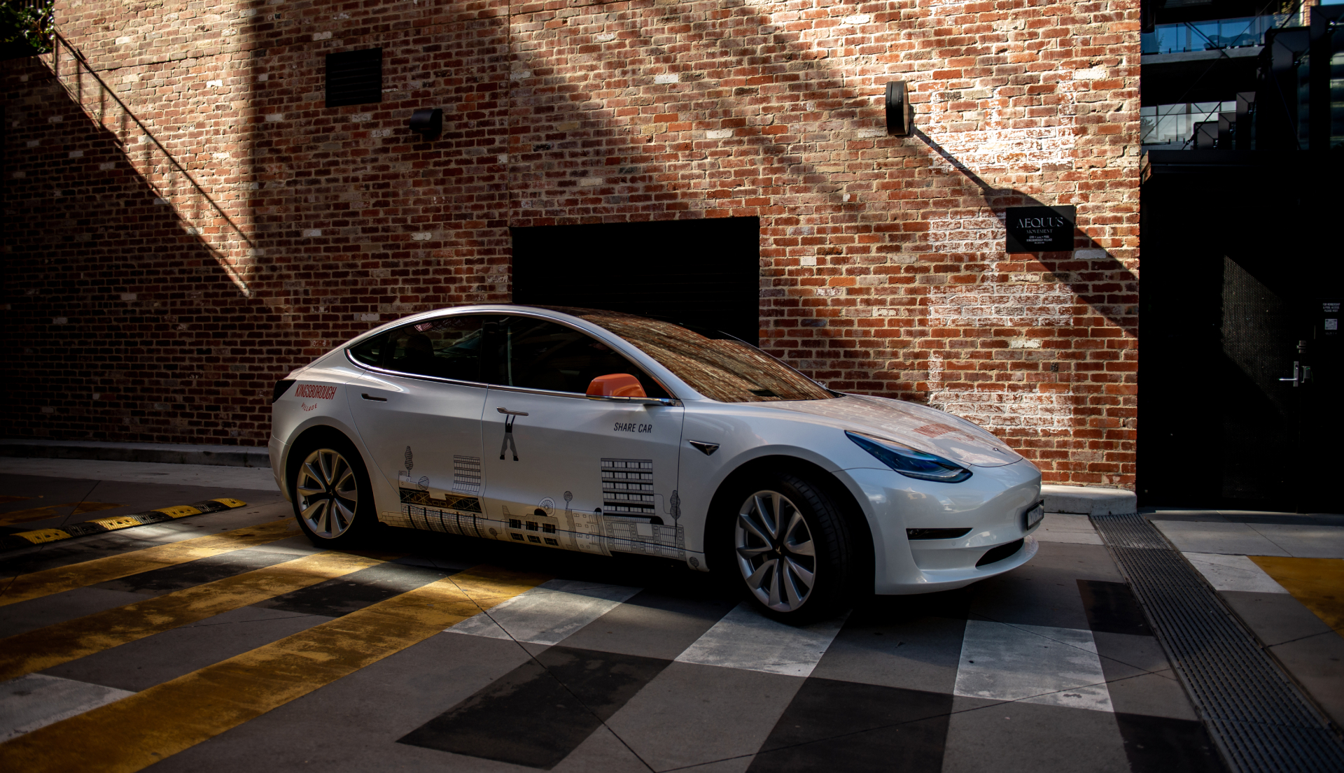 Kingsborough Branded Tesla car in front of Woolstrore brick building.