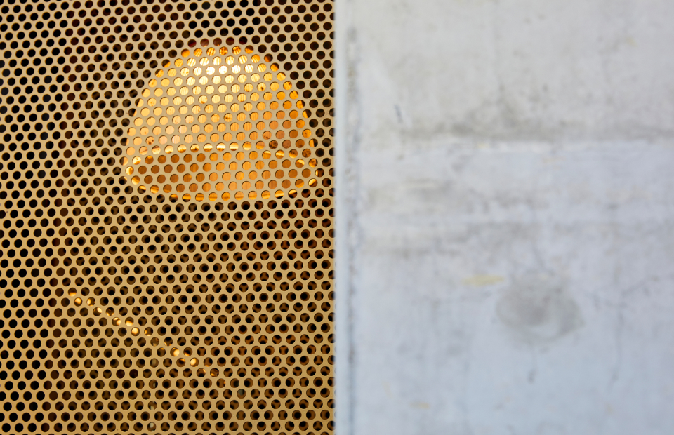 Wal made half of yellow mesh and half concrete. Through the mesh you can see an industrial style domed pendant light.
