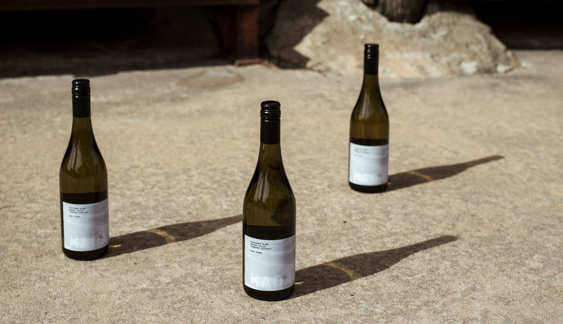 Three wine bottles on stone/concrete. Wine bottles are casting long shadows.