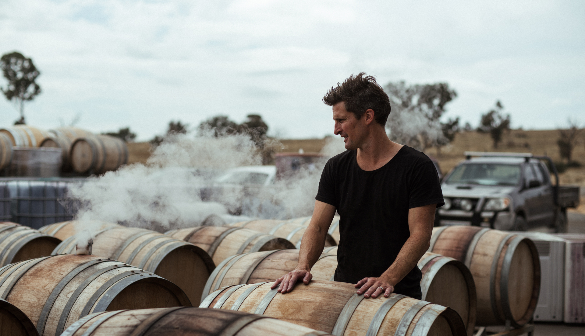 Winemaker standing outside amongst wine barrels that are being steamed.