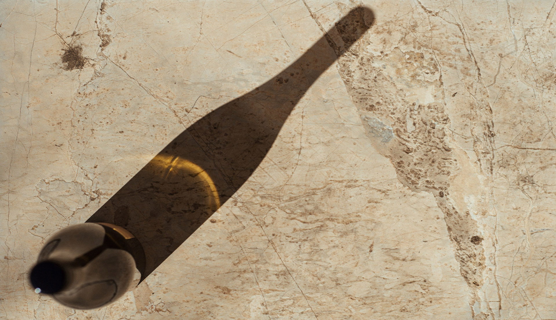 Wine bottle casting long shadow onto stone ground
