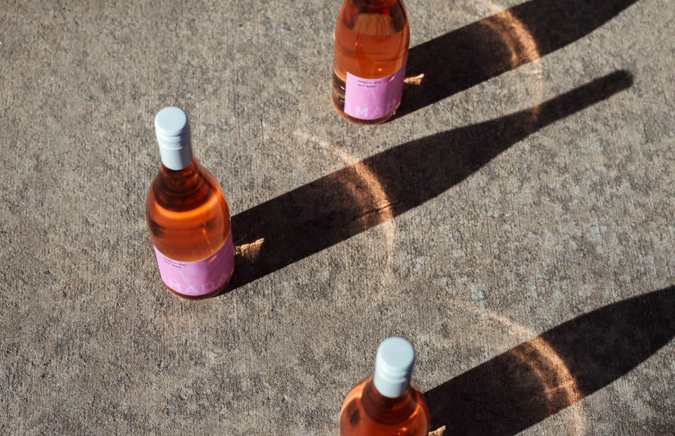 Three rose bottles on concrete ground. Sun is casting long shadows and light is shining through pink glass.