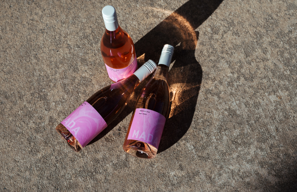 Three rose bottles on concrete ground. Sun is casting long shadows and light is shining through pink glass.