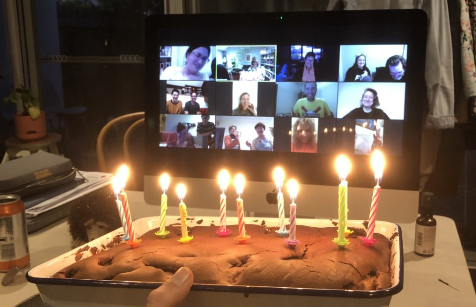 Photo of birthday cake with candles in front of computer with a zoom meeting on screen.