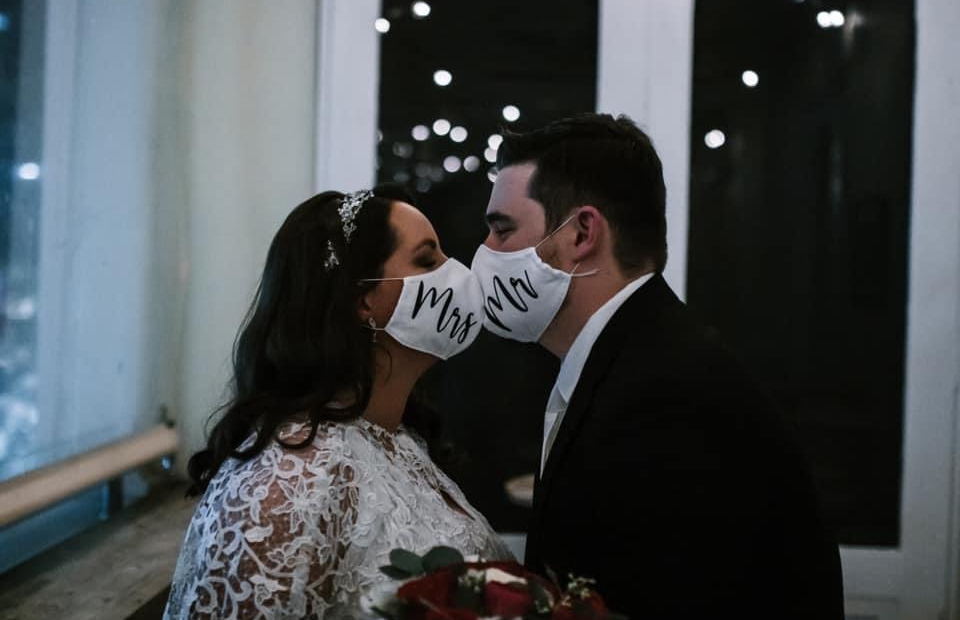 Photograph of bride and groom kissing while wearing face masks.