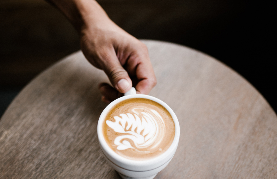 Hand holding a coffee cup with latte art picture of a swan