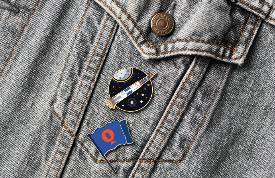 Two enamel pins (rocket and Questacon flag) on a denim jacket.